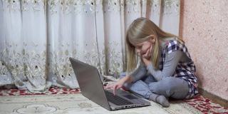 一个中学年龄的小女孩坐在家里的地板上使用笔记本电脑。远程学习时在键盘上打字。