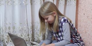 一个中学年龄的小女孩坐在家里的地板上使用笔记本电脑。用电脑做作业。