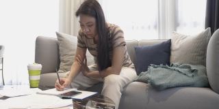 东南亚妇女工作在家庭财务，预算，在家里使用智能手机上的计算器近距离总计所有的每月家庭开支。女人为家庭理财