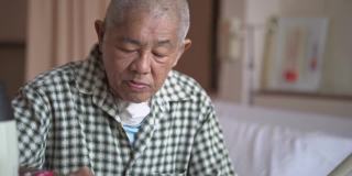 一位亚洲华人老年男病人坐在病房的床上吃早餐，在煎饼上涂黄油