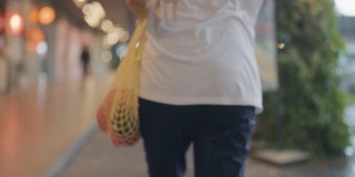 亚洲妇女行走在城市与可重复使用的袋子购物