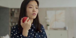 一个体贴的亚洲女人在客厅里拿着一个苹果，看着窗外