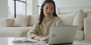 一位亚洲女性戴着耳机看着笔记本电脑屏幕，与对话者交流。韩国女商人戴着耳机视频呼叫客服