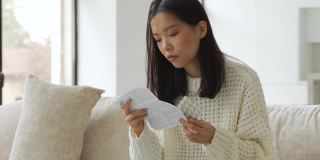 一位患感冒和流感的亚洲妇女坐在沙发上，手里拿着药片阅读说明