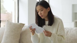 一位患感冒和流感的亚洲妇女坐在沙发上，手里拿着药片阅读说明视频素材模板下载