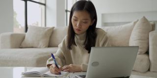 一位年轻的亚洲女学生正在使用电脑和平板电脑。一位年轻的女商人正坐在办公桌前，在笔记本上记着笔记。教育和技术的概念