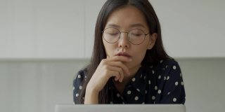 一位细心的亚洲女商人戴着眼镜，拿着笔记本电脑看着远方。学生使用虚拟电子学习资源