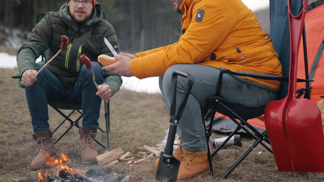 两个男人围坐在森林里的营火旁烤香肠