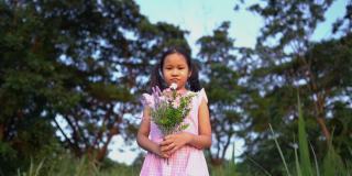 快乐的小女孩带着一束鲜花走过鲜花草地。快乐的小女孩在大自然中梦想。幸福的家庭,日落