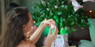 年轻的欧洲、亚洲和非洲女孩穿着家庭服装坐在圣诞树的地板上，拿着礼物庆祝圣诞节