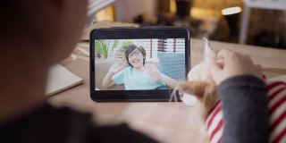 视频打电话给家庭社会距离概念，亚洲女性手势和问候她的儿子爱和幸福的谈话从平板电脑上与小狗朋友在线交谈