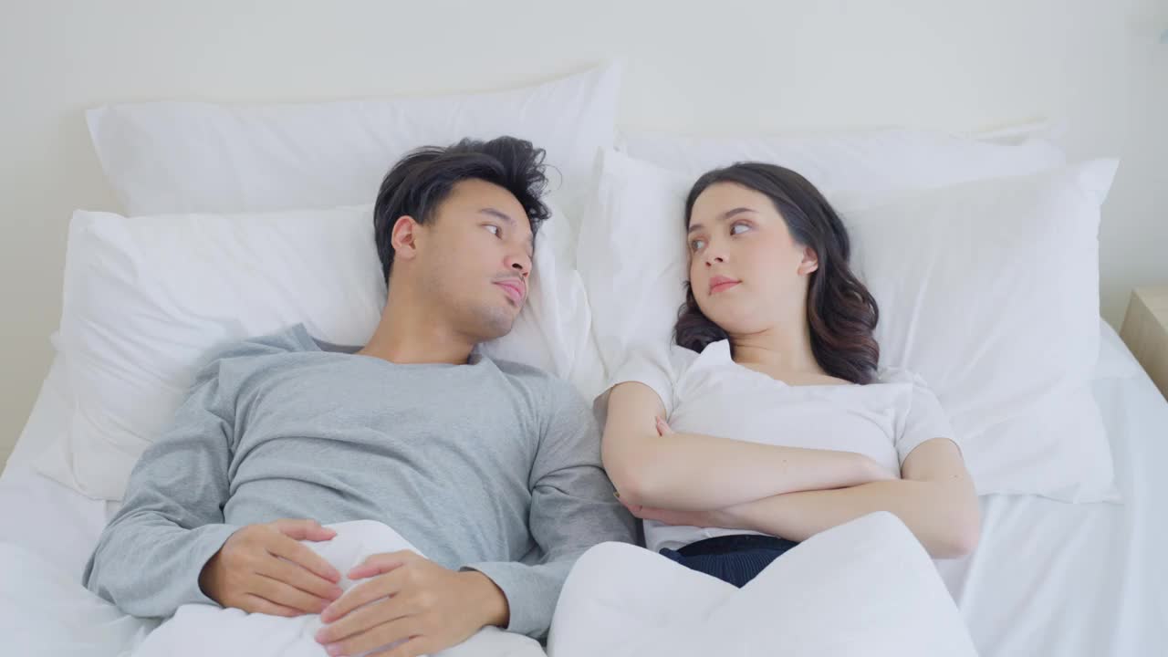 亚洲年轻夫妇躺在床上痛苦地争吵后。新婚男女为他们的争吵冲突而心碎，睡在卧室里。家庭problem-separation概念。