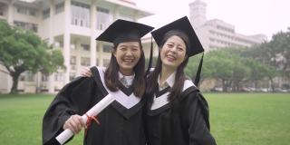 自拍回忆真实的时刻。两个开朗的亚洲毕业生自拍。迷人的女大学生最好的朋友穿着长袍和臼板在夏天的草地上。