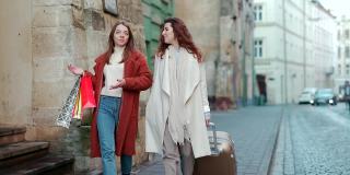 两个年轻的女游客走在老城区的街道上，提着一个手提箱和礼品袋