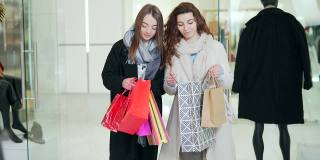 两个时尚的女孩在购物中心的服装店选购礼品袋。年轻成人快乐开朗的女性