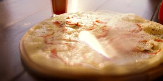 意大利披萨与切片蔬菜，融化的奶酪在前景。把奶酪放在烤披萨上的人。木制盘子上的典型意大利菜。开胃的披萨。Delisious菜