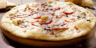 木盘上美味披萨的慢动作。白酱披萨，蕃茄，辣椒，鸡蛋在前景。意大利菜。背景中有一块奶酪。开胃菜