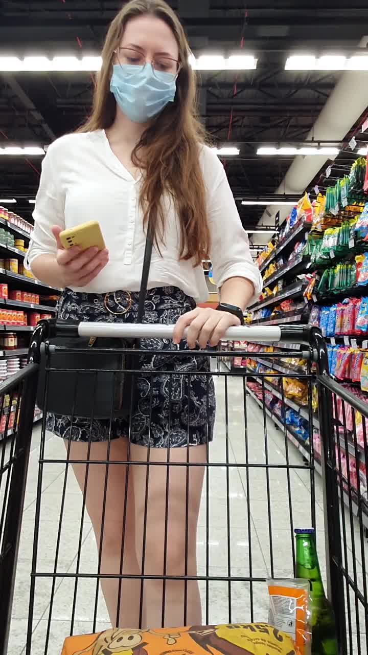 在超市购物时戴着防护口罩使用手机的妇女