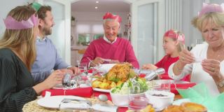 一家人戴着纸帽子，带着圣诞饼干带来的礼物，坐在餐桌前一起吃饭