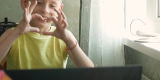7 ~ 9岁的白人男孩在笔记本电脑前与正在进行视频通话的对话者愉快地打招呼。在互联网上进行在线交流和会议。无线家庭沟通