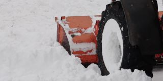 冬天，一辆带着黄色铲斗的拖拉机在街上铲雪。道路清扫援助。慢动作