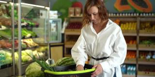 一名年轻女子站在超市货架的背景下，在菜篮子里挑选水果和蔬菜。