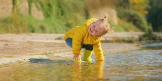 一个穿着黄色胶靴的小女孩小心翼翼地在河上走着。缓慢的运动。跟随拍摄