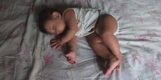 婴儿躺在床上，睡觉时打哈欠伸懒腰，正要醒来。前视图。