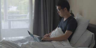 一个在酒店床上工作的亚洲人。从任何地方工作的概念。Workation。