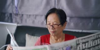 老妇人坐在沙发上看报纸。