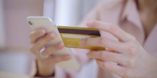 年轻的亚洲女子在公寓用手机用信用卡购物。在网上买东西和礼物