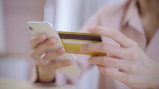 年轻的亚洲女子在公寓用手机用信用卡购物。在网上买东西和礼物视频素材模板下载