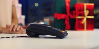 近距离拍摄一名男子在假日商店用NFC技术购买圣诞礼物，pos终端上有智能手机信用卡应用程序。
