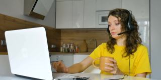 一名年轻女子正在用她的笔记本电脑进行在线会议，一名女商人坐在公寓的厨房里，带着数字平板电脑，客户经理，在户外工作，远程工作，支持