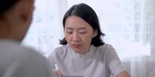 一位亚洲女性在家里的客厅里用平板电脑和朋友聊天。靠近年轻少女的脸时分享工作给她的朋友看。人们在家工作。