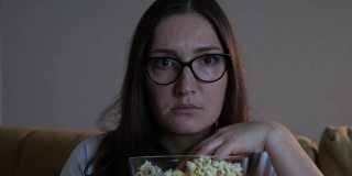 一脸恐惧的女士一边看恐怖电影一边吃爆米花