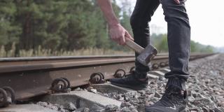 一个戴着头盔的铁路工人正在修理铁路，用大锤敲打着铁路的塔尖。