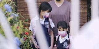 回到学校的亚洲华人母亲送她的两个女儿上学从家在前院的房子防护口罩