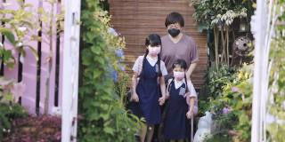 回到学校的亚洲华人母亲送她的两个女儿上学从家在前院的房子防护口罩