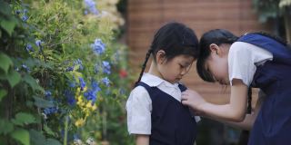 回到学校的亚洲华人姐姐在早上从家到学校的前院里帮妹妹戴上校名标签徽章