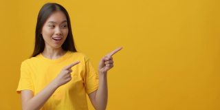 兴奋的中国女人一边手指一边竖起大拇指，黄色背景