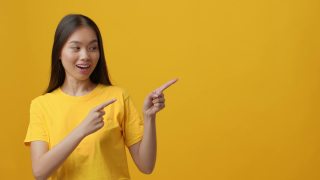 兴奋的中国女人一边手指一边竖起大拇指，黄色背景视频素材模板下载