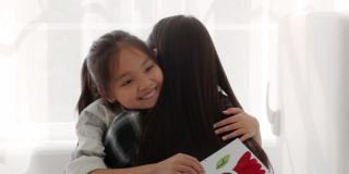 亚洲女孩抱着妈妈，手里拿着明信片祝贺家里的妈妈