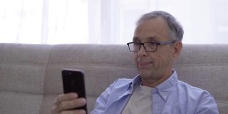 50-60岁的老人微笑着看着智能手机屏幕。