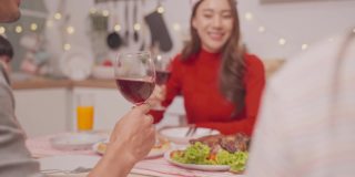 亚洲幸福家庭，年轻夫妇一起在家里举办圣诞晚会。漂亮迷人的父母在餐桌上碰杯，吃晚餐庆祝圣诞节的晚上在家里。