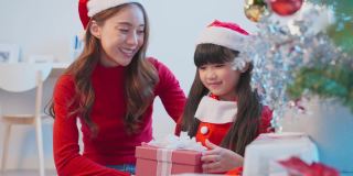 亚洲可爱的小女儿打开父母送来的礼物盒。幸福的家庭，小屁孩感到幸福和兴奋的惊喜来自妈妈和爸爸准备在家里一起庆祝圣诞节