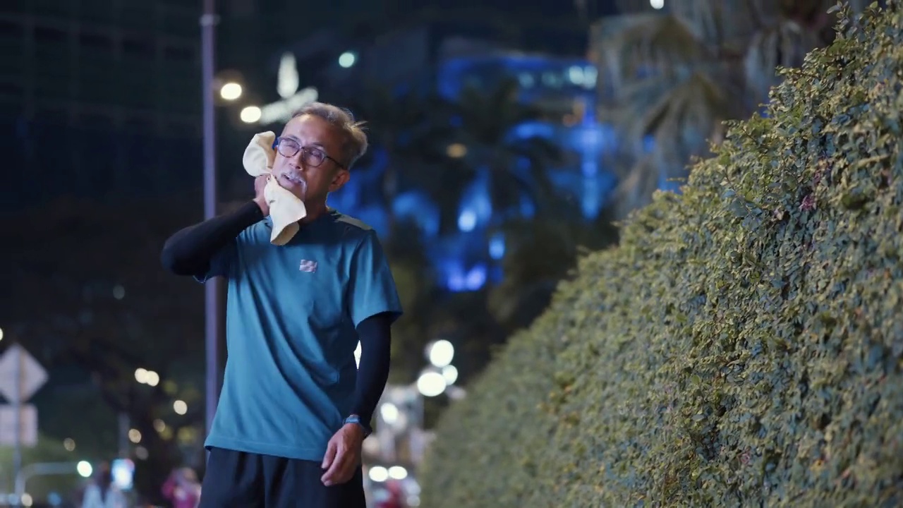 晚上下班后，在城市慢跑后，一名亚裔中国活跃老人用毛巾擦汗