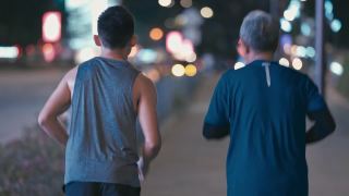 后视图亚洲华人活跃的老人和儿子晚上下班后一起在城里跑步慢跑视频素材模板下载