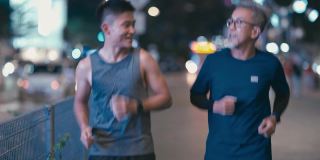 亚洲华人活跃的老人和儿子晚上下班后一起在城里跑步慢跑