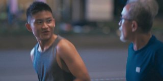 侧观亚洲华人活跃的老人和他的儿子晚上下班后一起在城市跑步慢跑